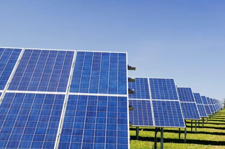 Row of ground-mounted commercial solar panels angled toward a clear blue sky.